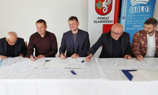 beneficjenci siedzą za stołem, podpsują umowy, w tle biała ściana